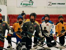 Young kids in various colourful hockey jerseys kneeling and listening to the coach on the ice at Hockey Etcetera's Mentorship camp.